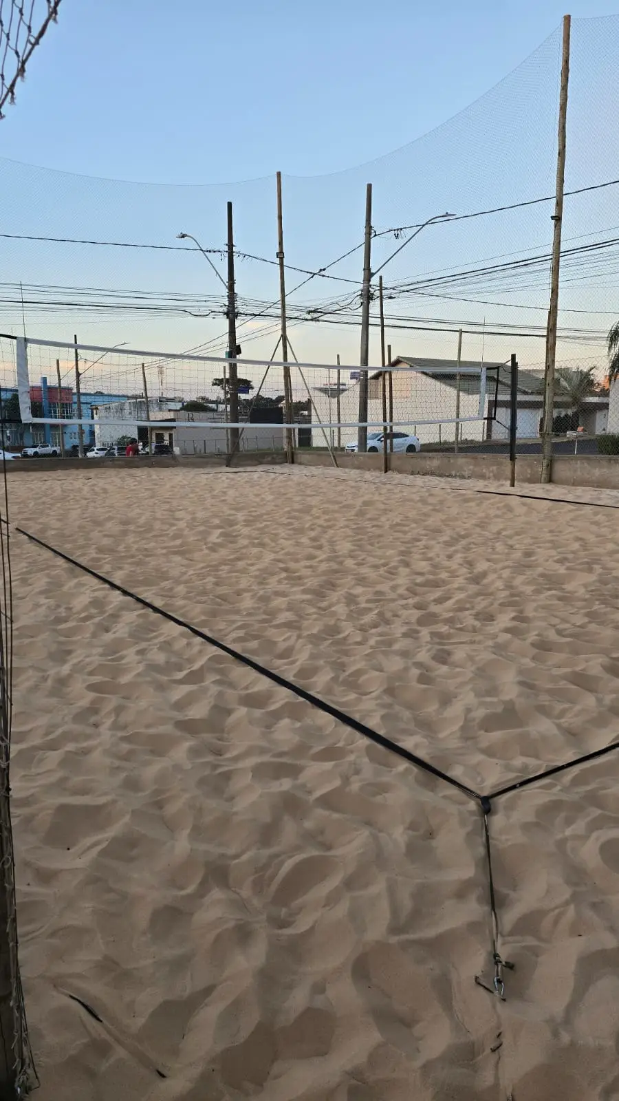 Quadra de areia com as linhas marcadas, cercada pela tela de proteção