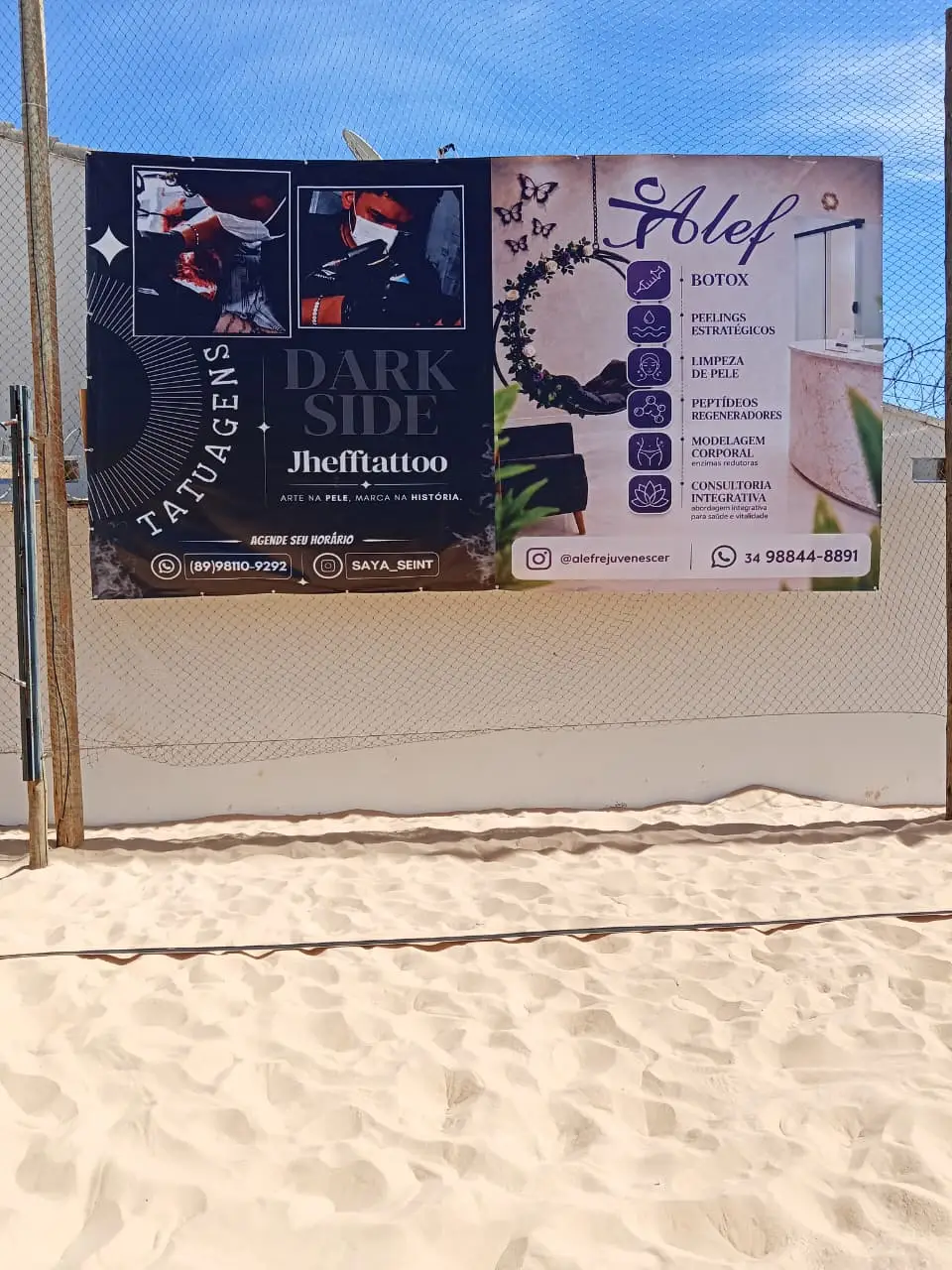 Dois banners de empresas presos na tela de proteção, acima da areia da quadra
